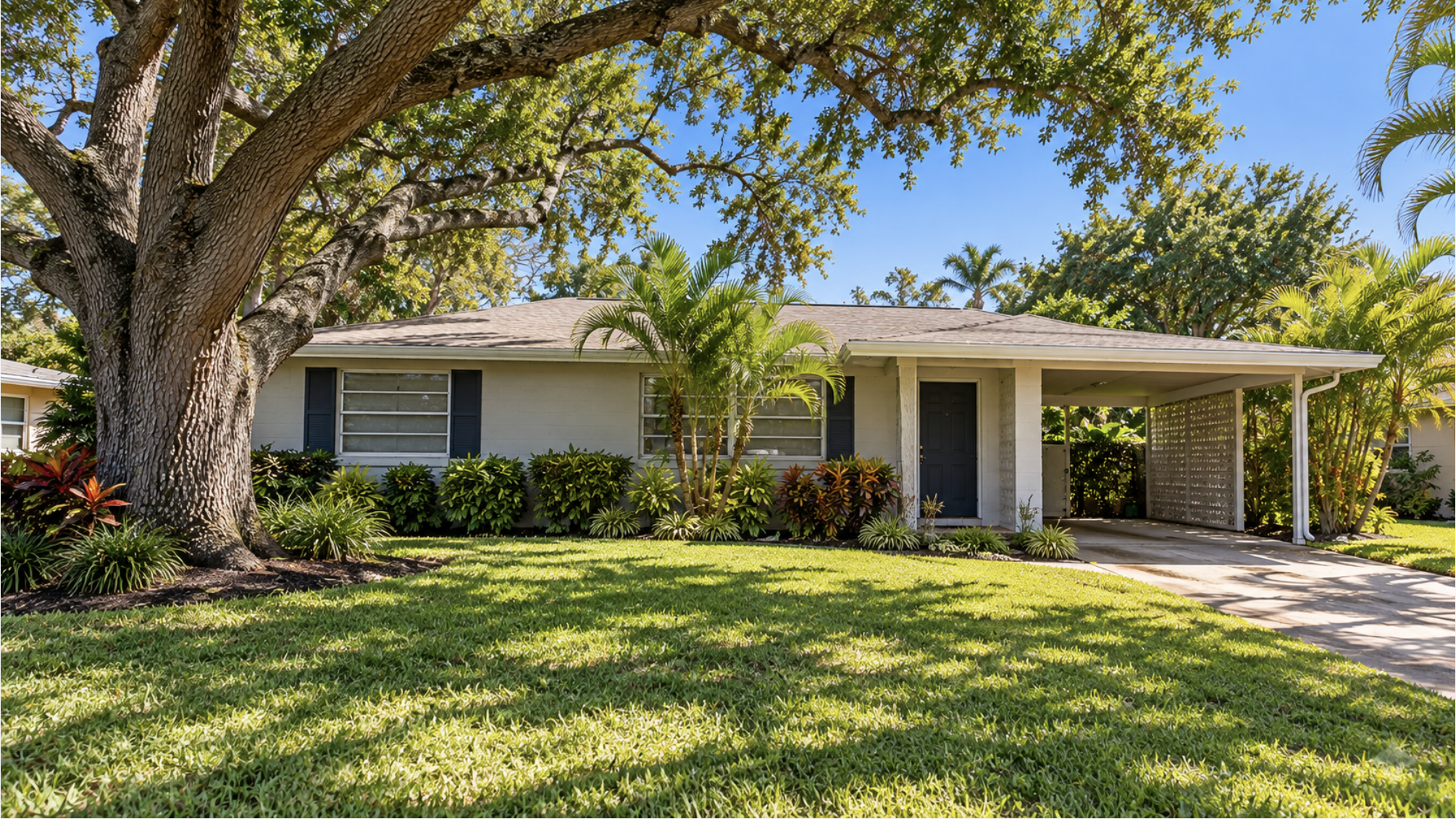 Single-story concrete-block ranch home with a carport and mature oak shade, the kind of 1960s and 1970s housing stock found across much of West Bradenton
